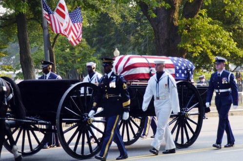 Military officer honors National Cemetery caisson flag draped casket.